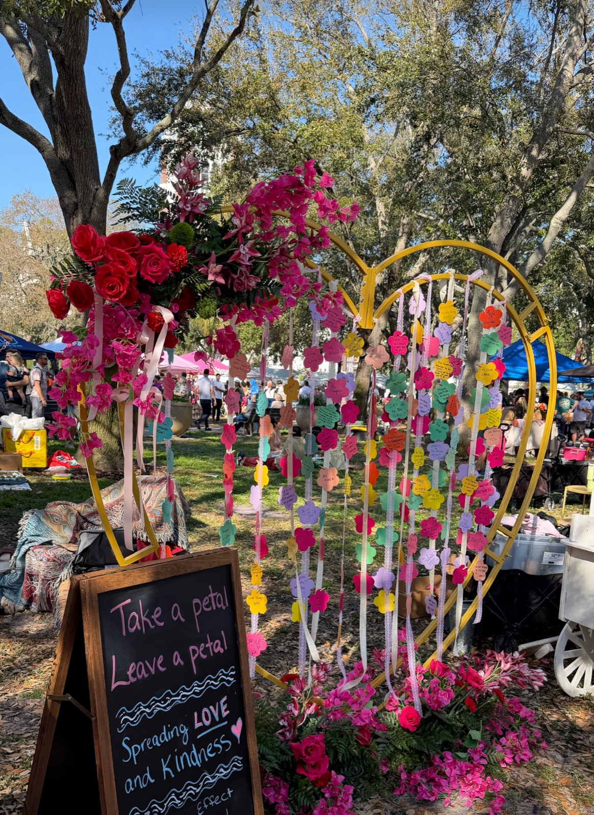 A heart of fresh flowers in a St. Pete park, with a sign reading: Take a petal, leave a petal